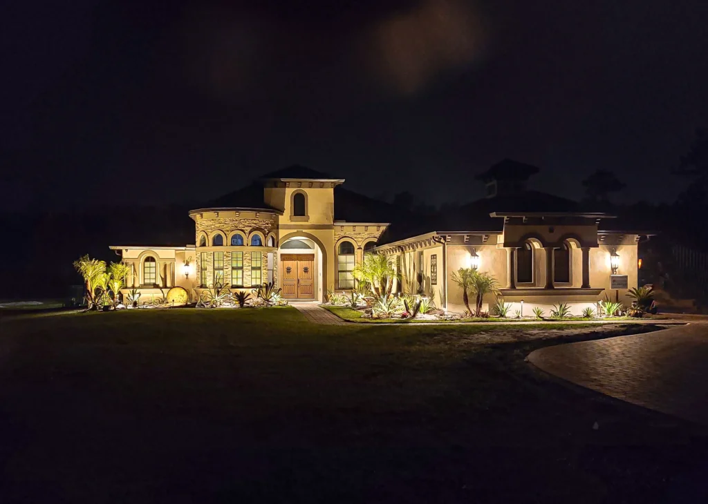 Warm LED landscape lighting on a Mediterranean-style home in Gainesville, FL—uplighting palms, entry, and stucco façade.