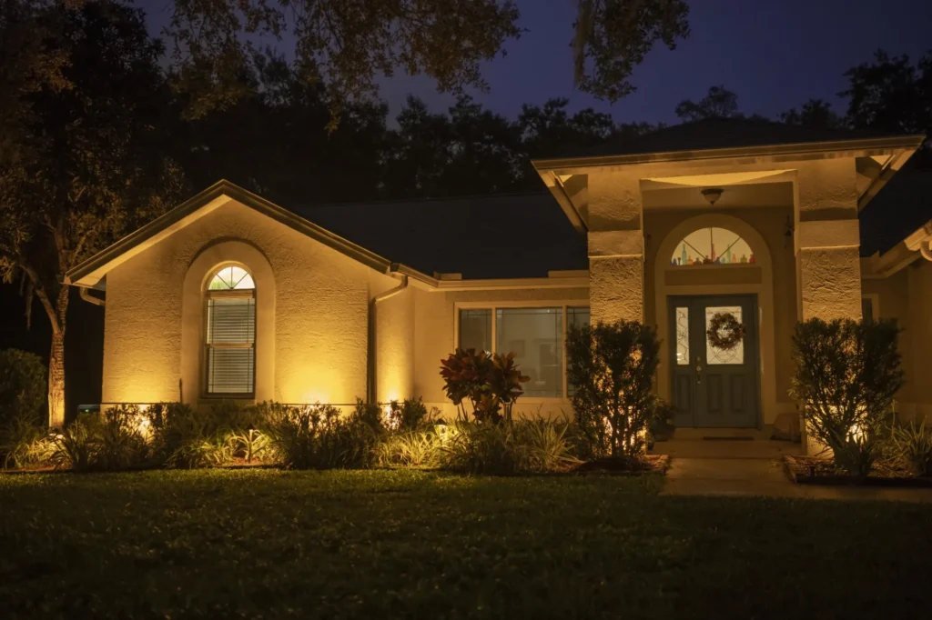Warm LED landscape lighting on a Gainesville, FL home—uplights highlighting entry columns, shrubs, and facade for curb appeal.