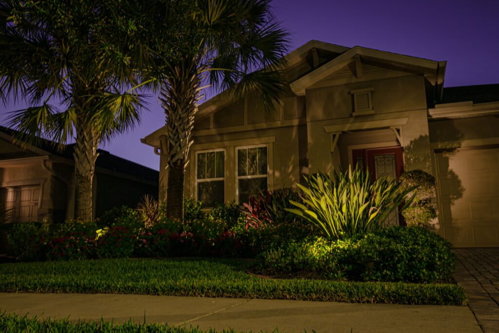 Warm LED uplighting on front entry, palms, and garden beds at a Newberry, FL home